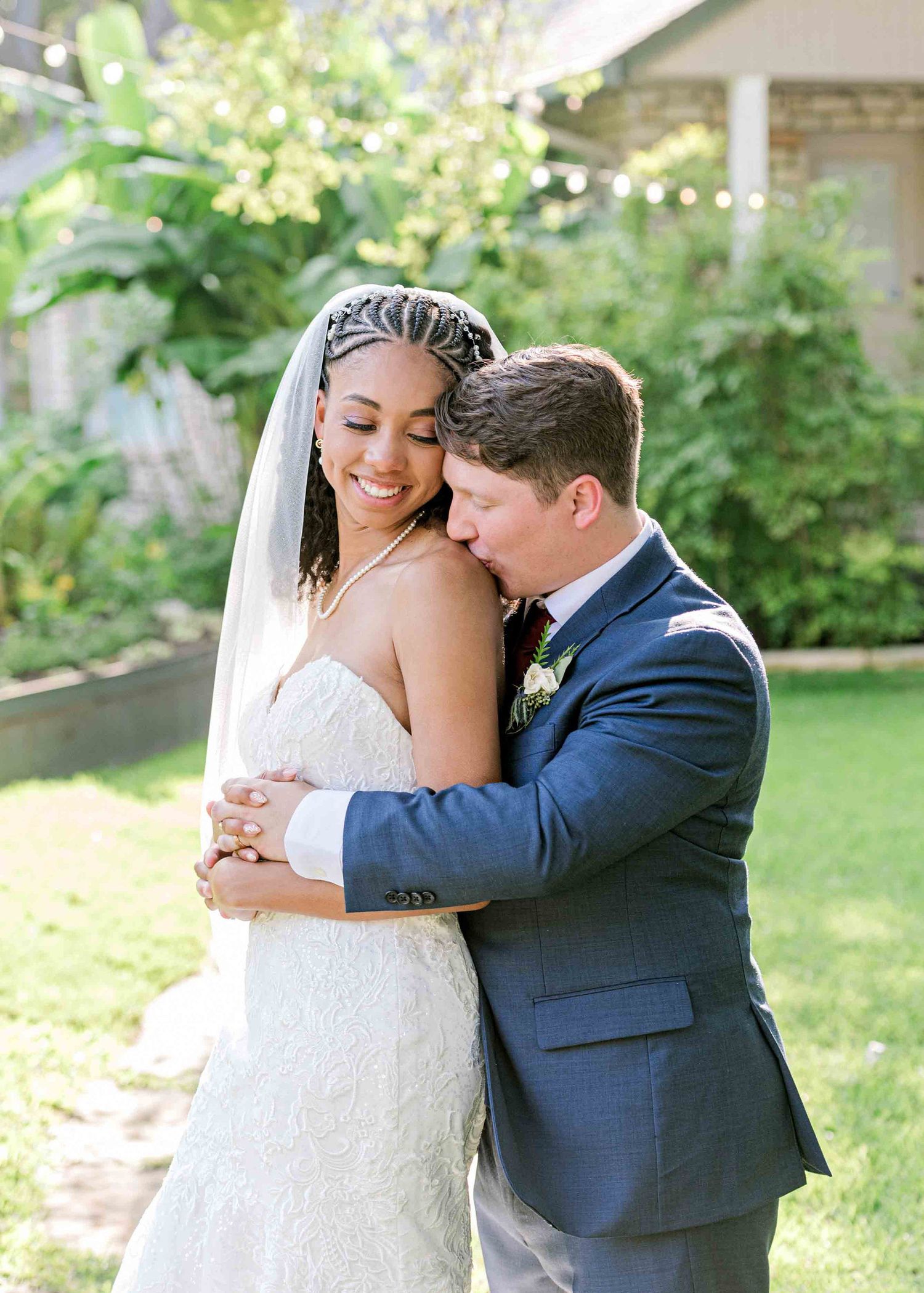 Newlyweds share an intimate moment in a garden setting with string lights and greenery.