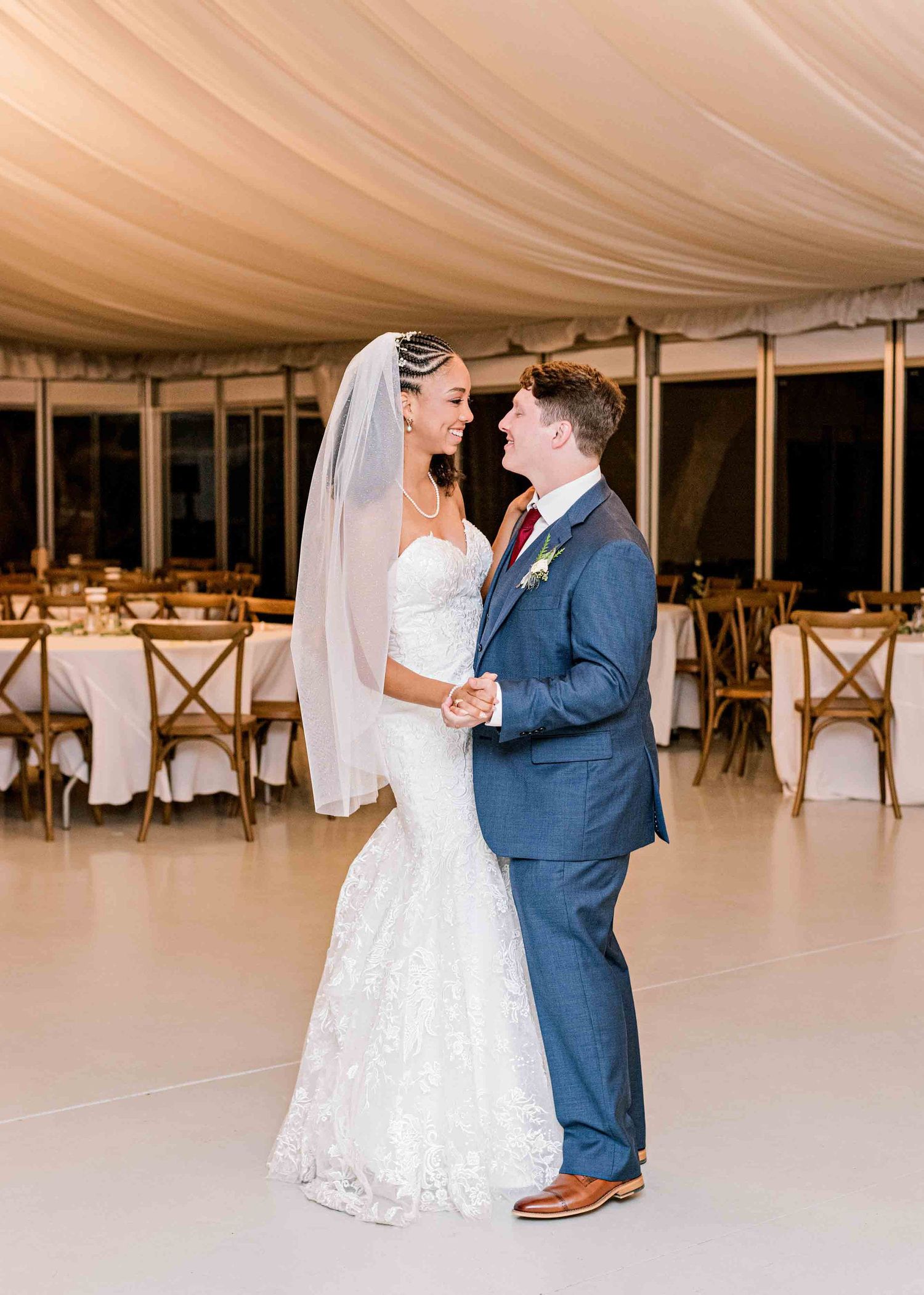 Newlyweds sharing an intimate dance moment under elegant draped ceiling and chandeliers.