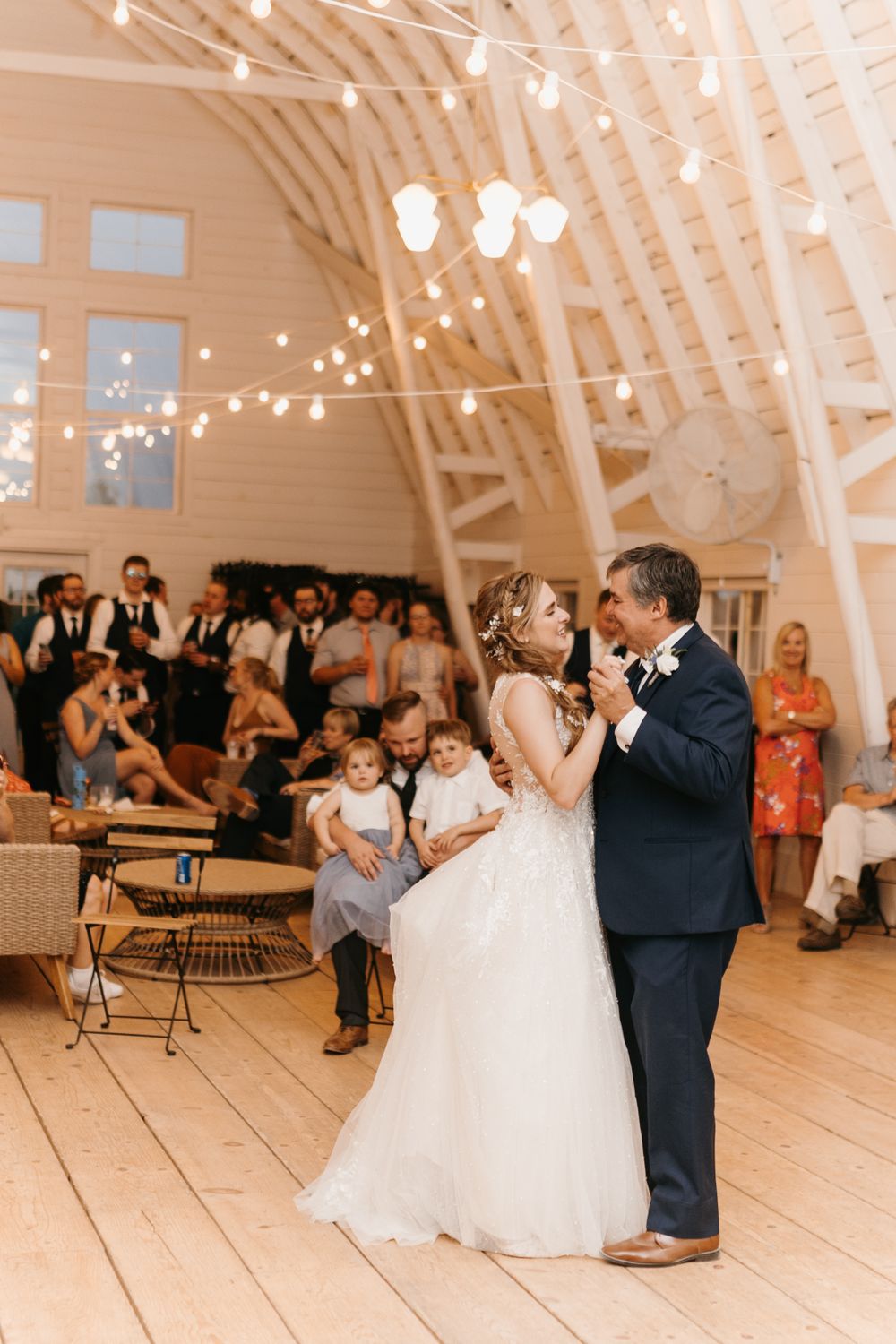 Bride shares a special father-daughter dance under warm string lights at a rustic barn wedding reception.