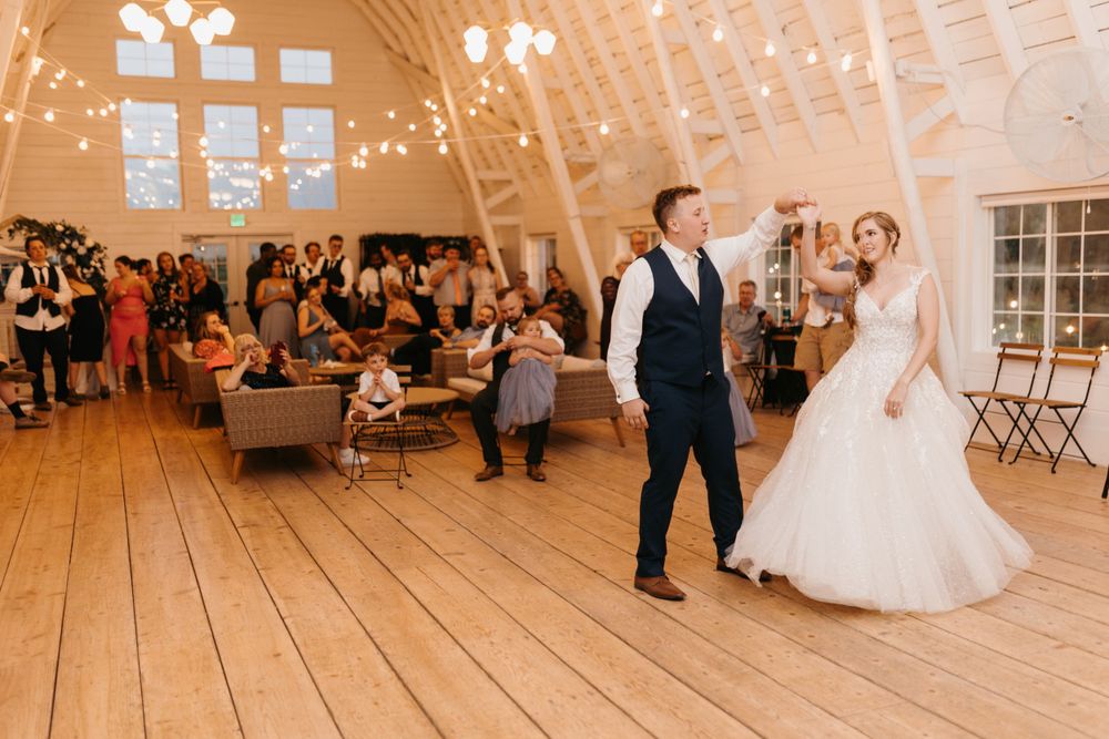 Bride and groom share their first dance in a charming barn wedding venue with string lights overhead.