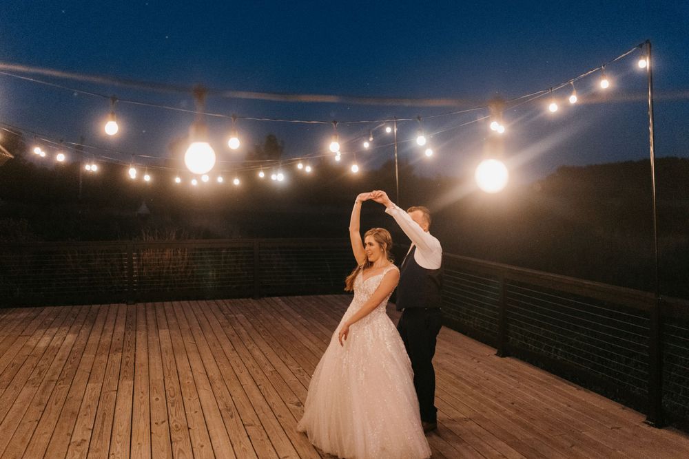 Bride in a tulle gown twirls during first dance under string lights on a rustic outdoor deck.