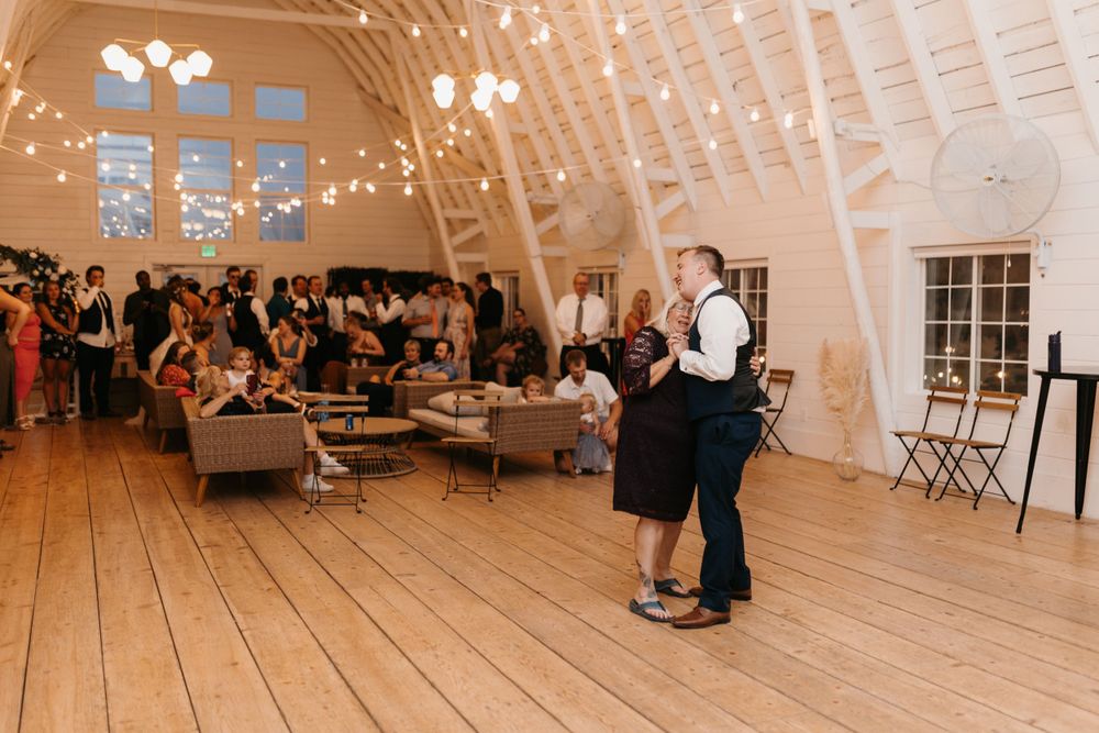 Wedding guests watch as a couple shares a dance on the wooden floor of a rustic barn reception venue.
