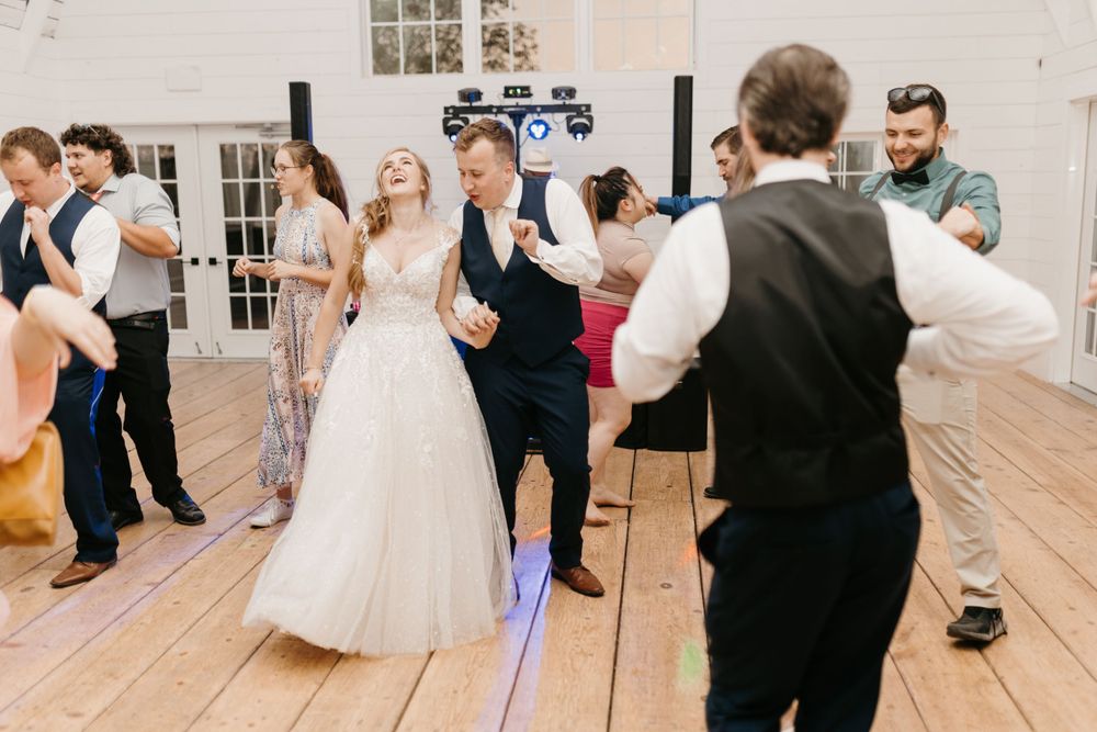 Bride laughing and dancing with groom surrounded by celebrating guests on a wooden dance floor.