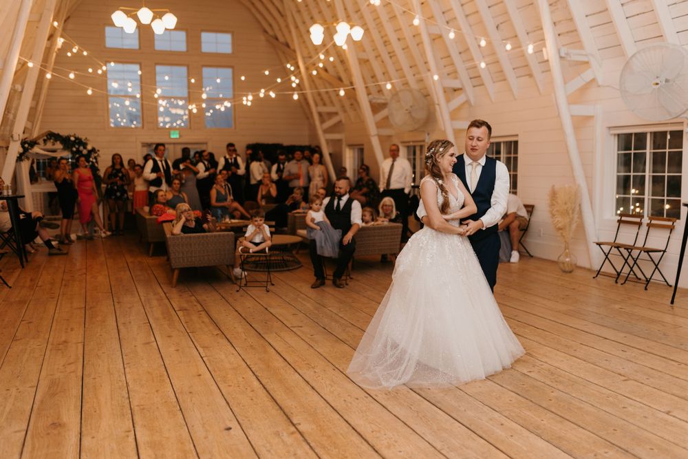 Bride and groom share an intimate first dance under string lights in a rustic barn wedding venue.