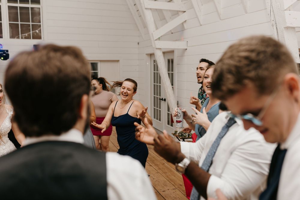 Wedding guests laughing and dancing together joyfully on the dance floor during reception celebration.