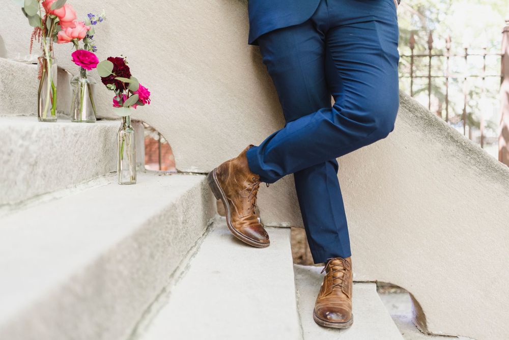 Brown leather shoes and navy suit details against light colored background.