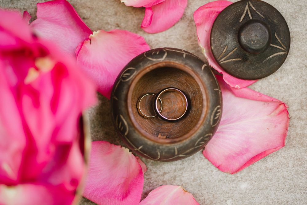 Wedding rings nestled in a wooden holder surrounded by pink rose petals.