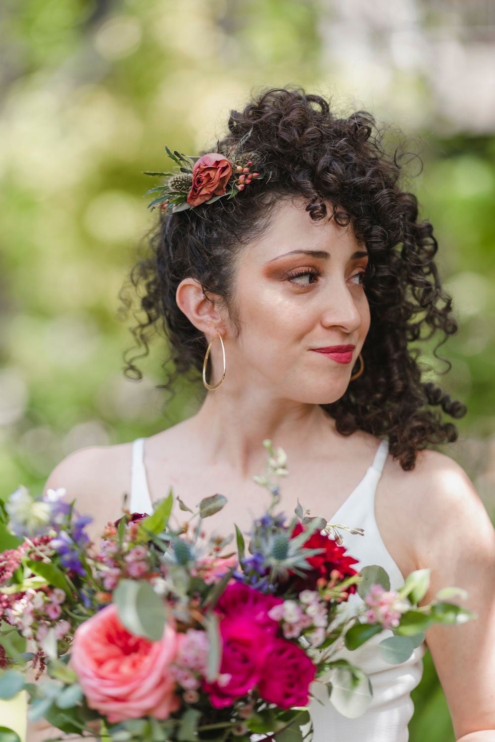 A bride holding a vibrant bouquet of pink and red flowers with greenery.