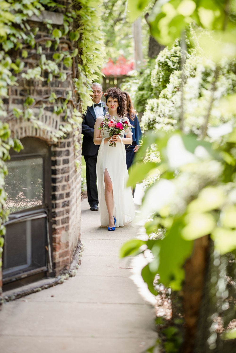 A couple walking down a garden path lined with climbing vines and white flowers.