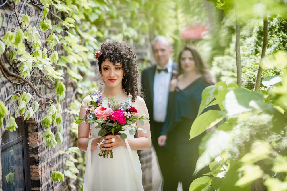 A wedding scene in a lush garden setting with brick walls and climbing vines.