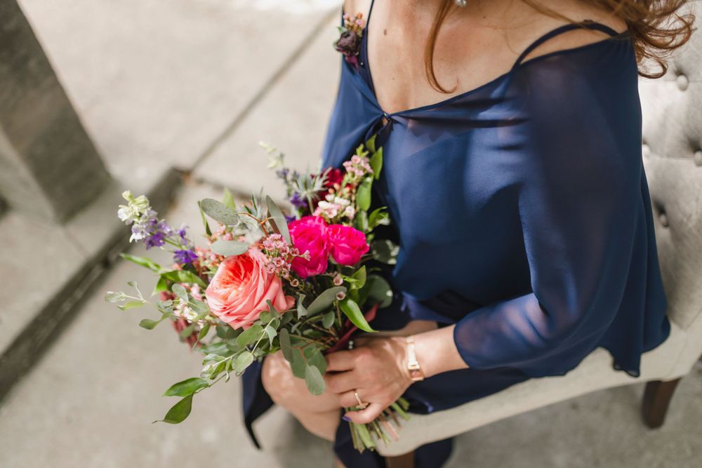 Person holding a colorful wedding bouquet with pink roses and purple flowers.