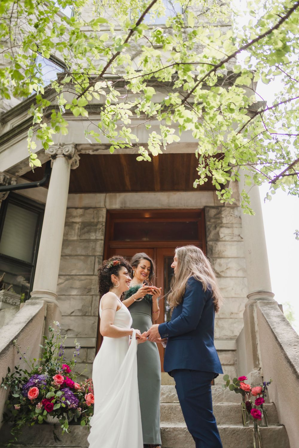 Wedding ceremony taking place on stone steps with spring blossoms overhead.