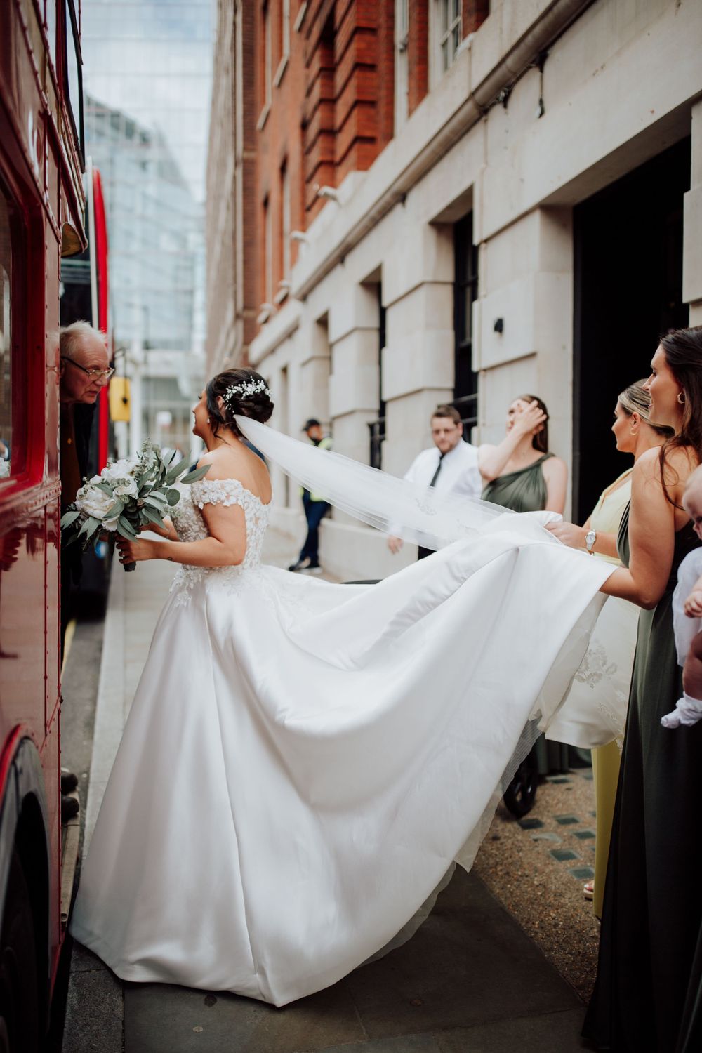 A flowing white wedding dress train being held by attendants on an urban street.