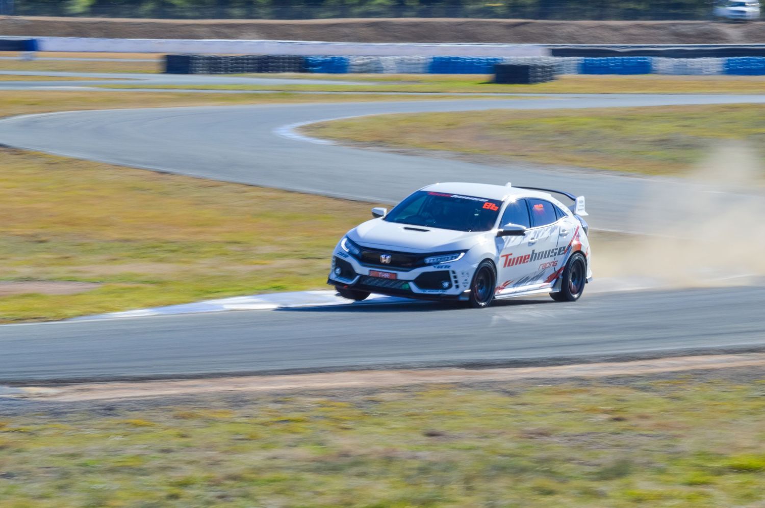 A Honda Civic Type R races around a track kicking up dust during a performance driving event.