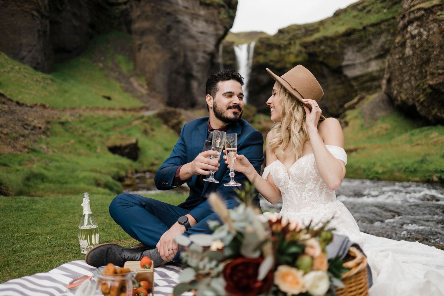 A romantic picnic by a waterfall with wine and charcuterie spread on a blanket.