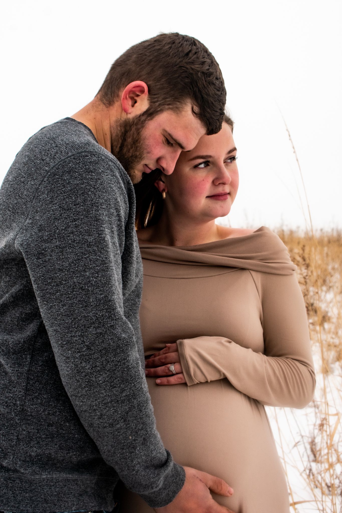 A tender maternity moment captured in winter with a couple in casual attire embracing and cradling a baby bump.