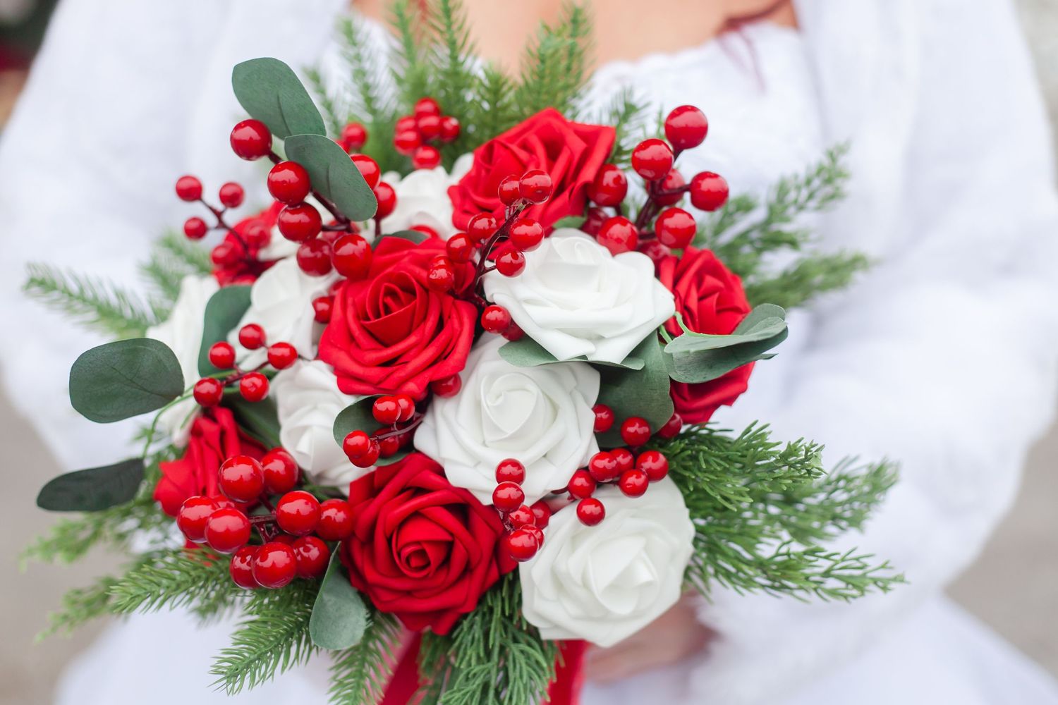 Red and white roses with berries and evergreen create an elegant winter wedding bouquet.
