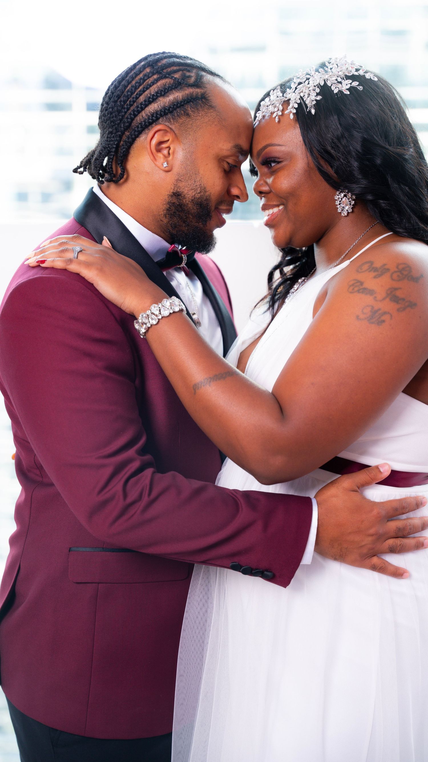 A wedding couple sharing an intimate moment, bride in white dress and groom in burgundy jacket.