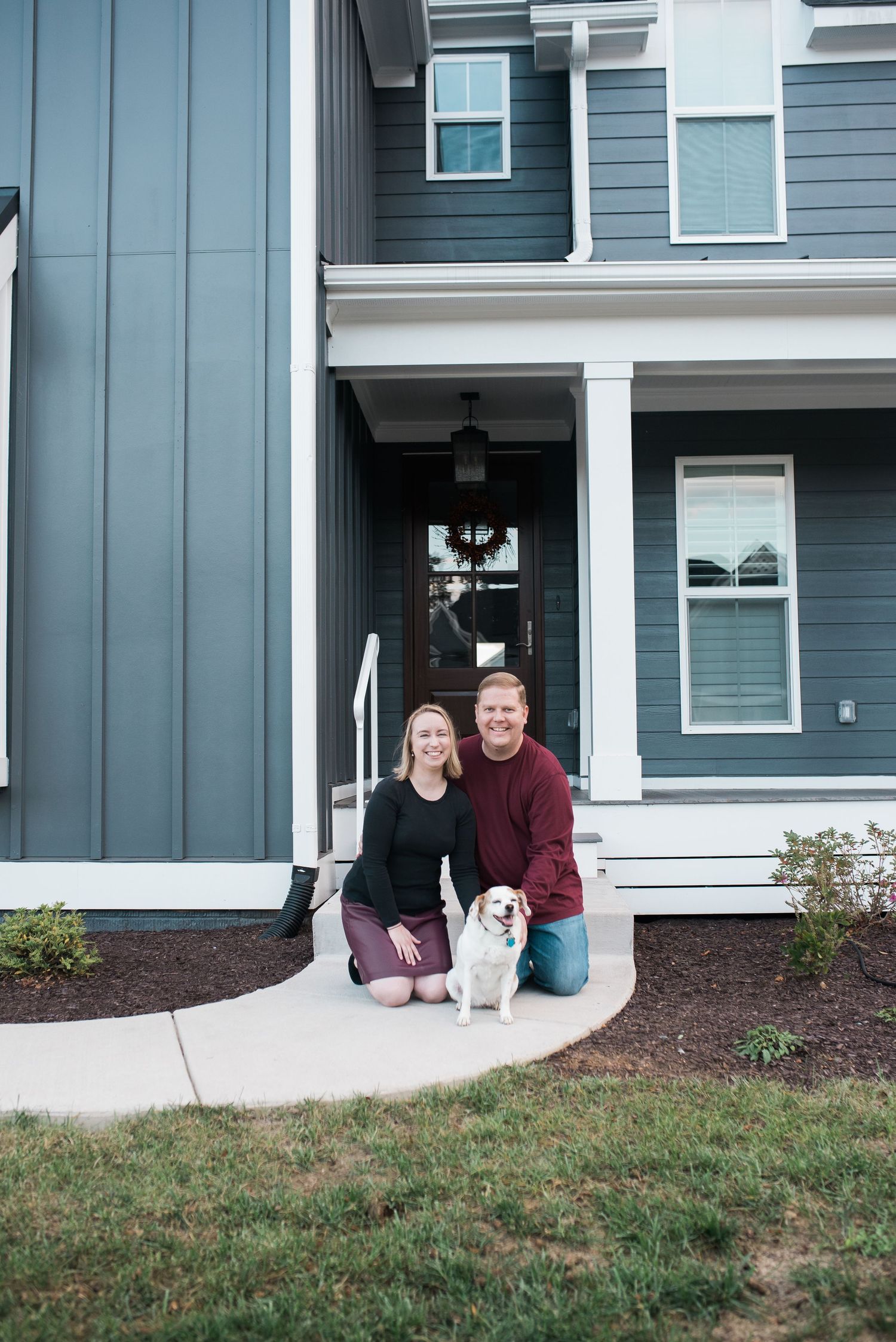 Couple poses with their dog on front porch of modern blue house.