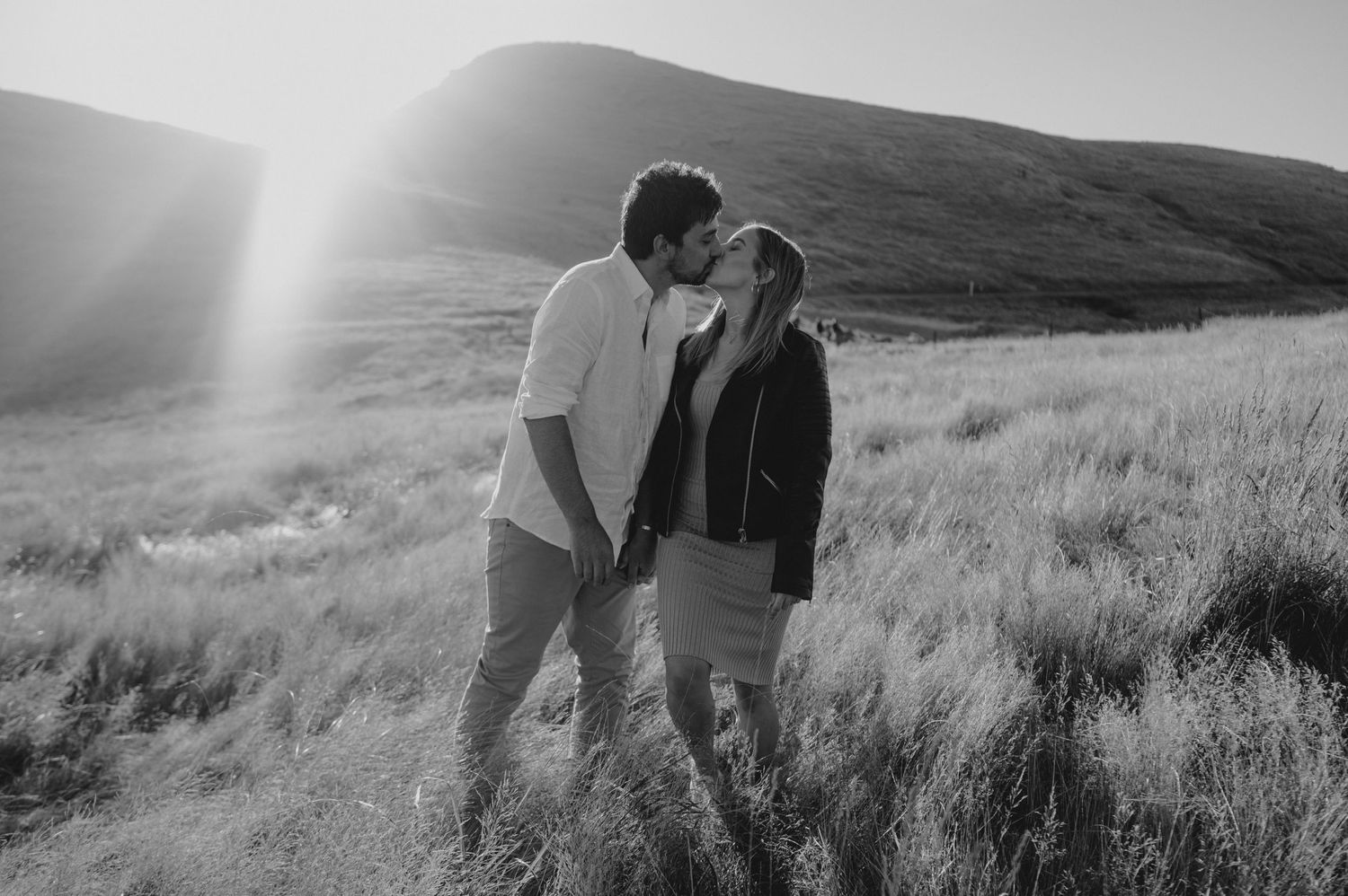 Romantic couple sharing a tender moment in a sunlit meadow with rolling hills in the background.