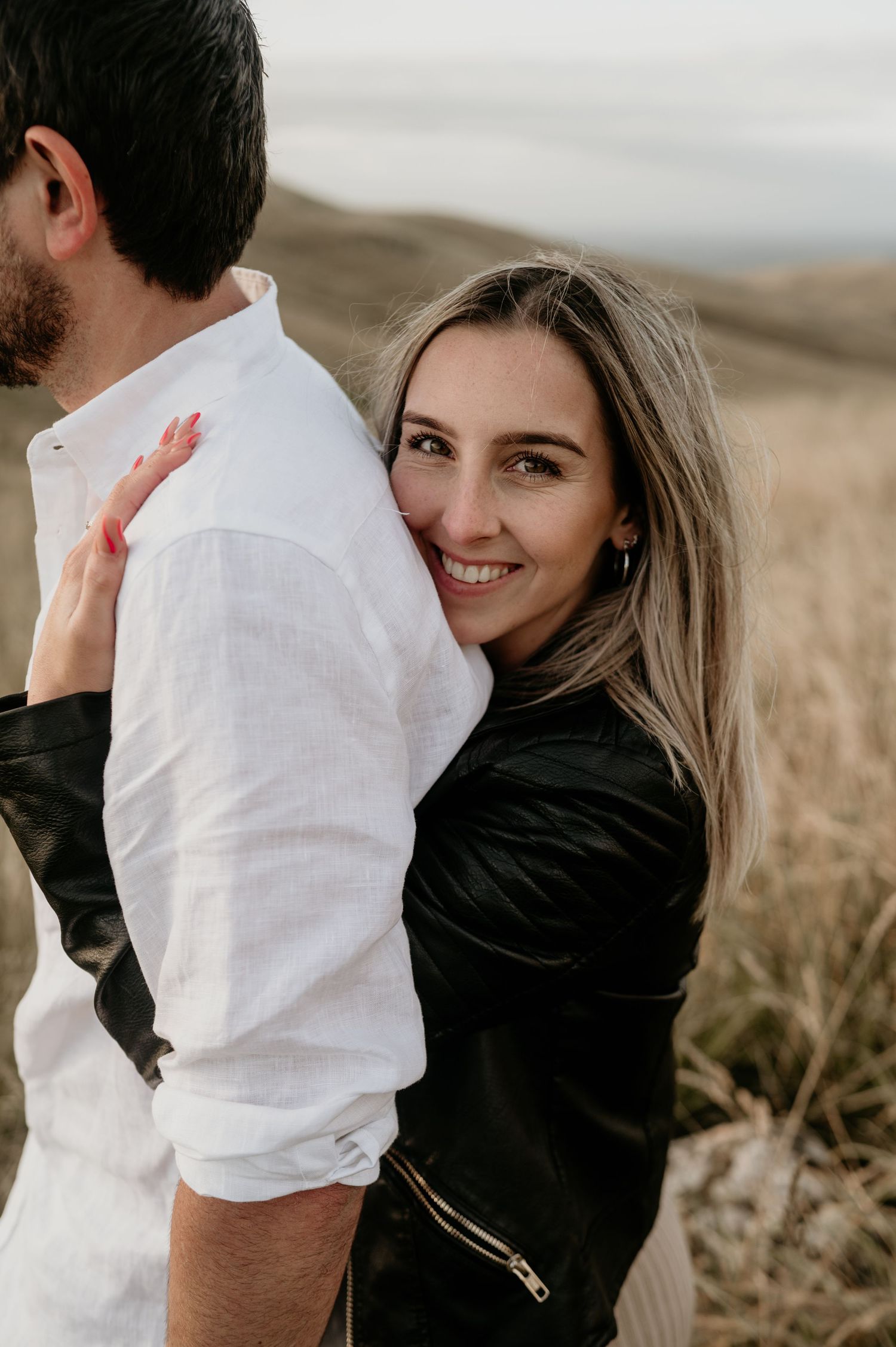 Happy couple embracing outdoors in a field with natural lighting and scenic backdrop.