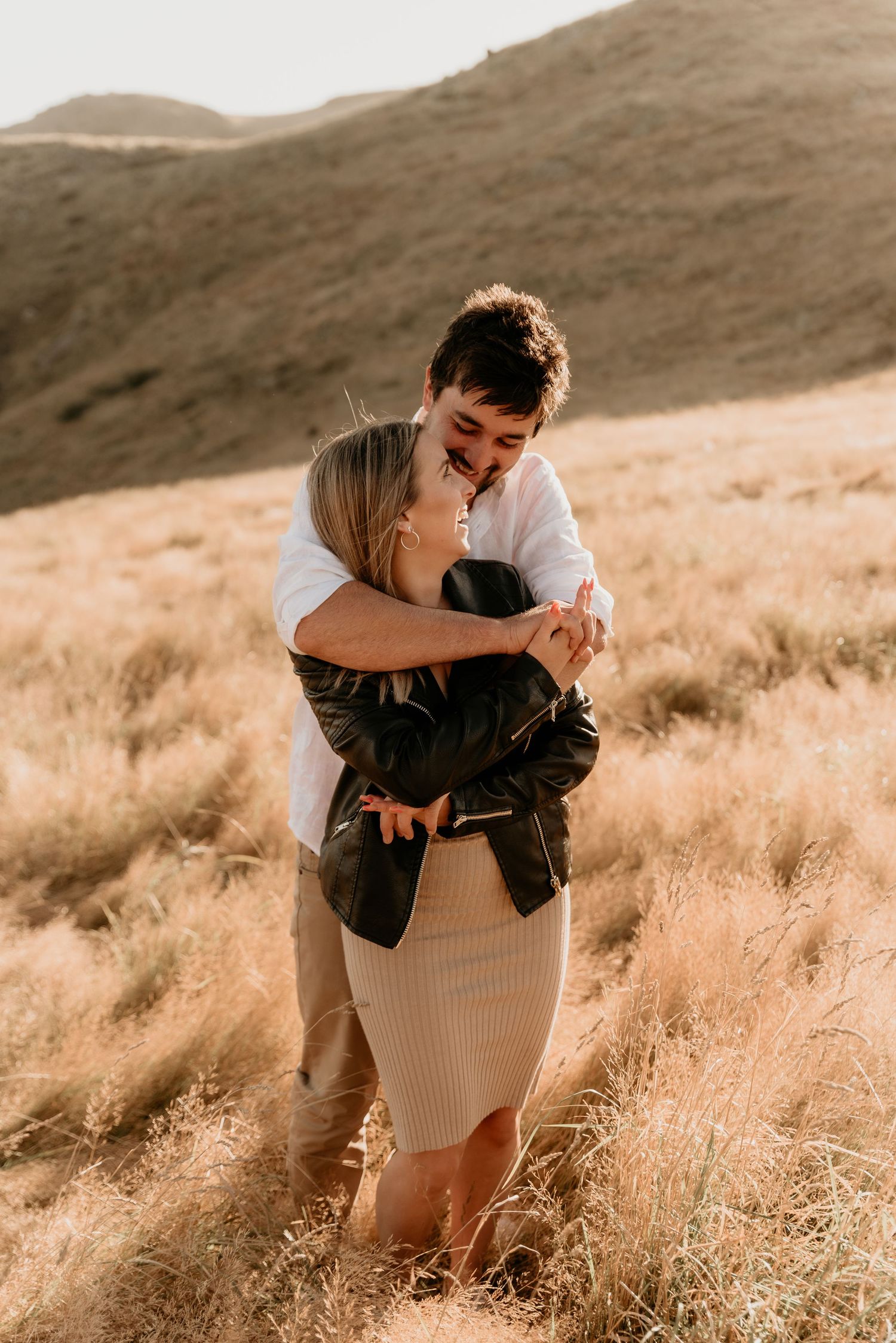 Joyful moment captured between couple laughing together in sun-kissed mountain field.