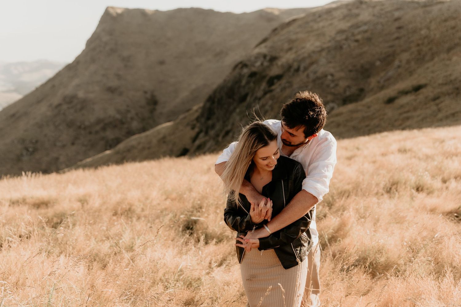 Intimate couple moment captured in warm sunlight on mountainside with scenic valley view.