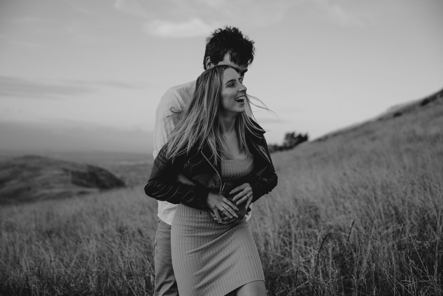 Intimate black and white portrait of couple embracing on hillside at dusk.