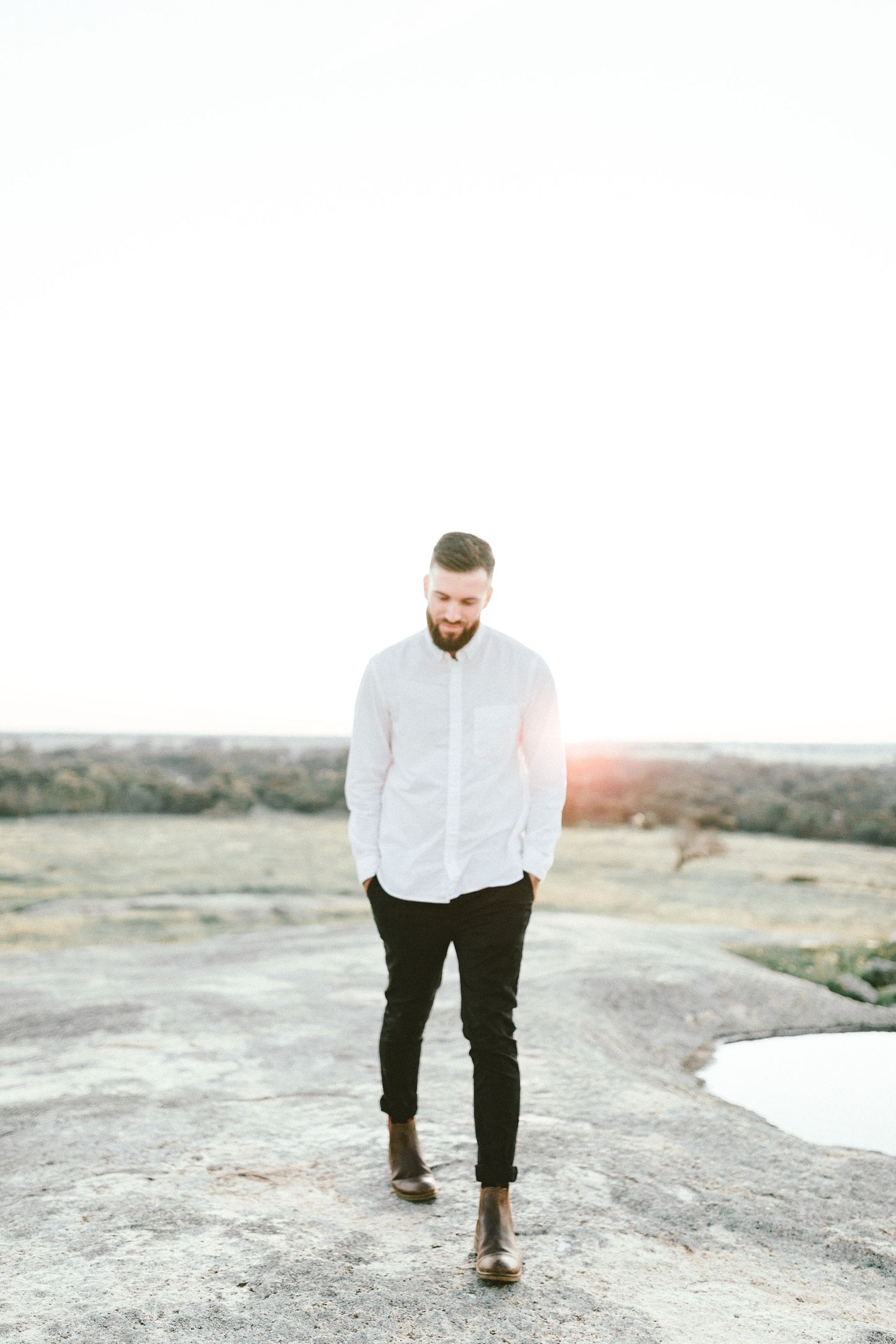 A person in white shirt and black pants walking on rocky terrain at sunset.