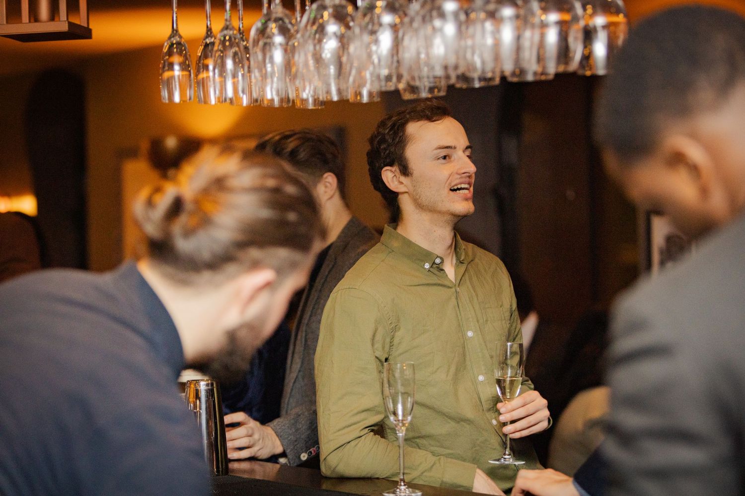 People enjoying drinks and conversation at a bar with hanging glass fixtures above.
