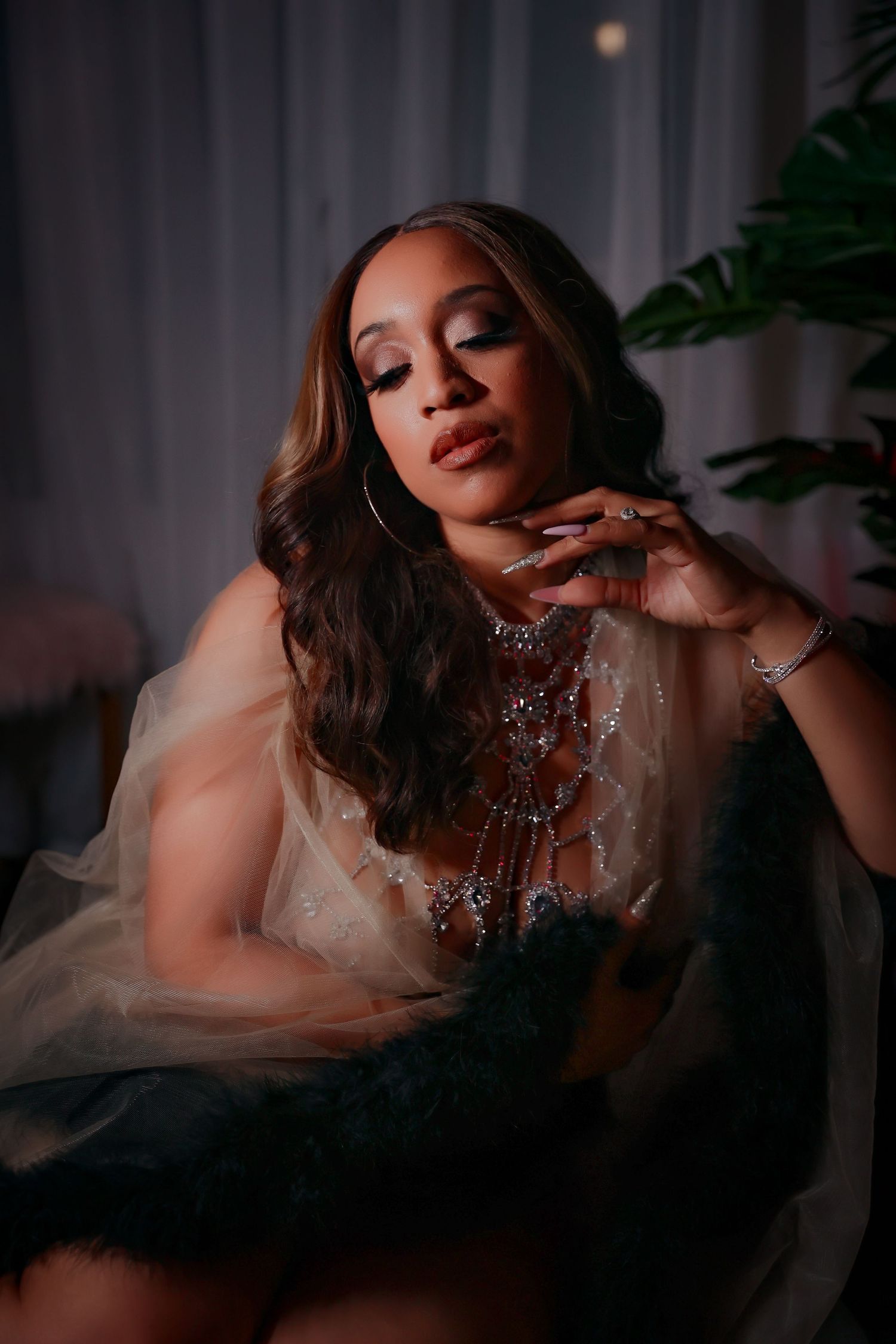 Glamorous boudoir portrait featuring owner of Photography By Kymisha wearing sparkly jewelry and sheer fabric in moody lighting.