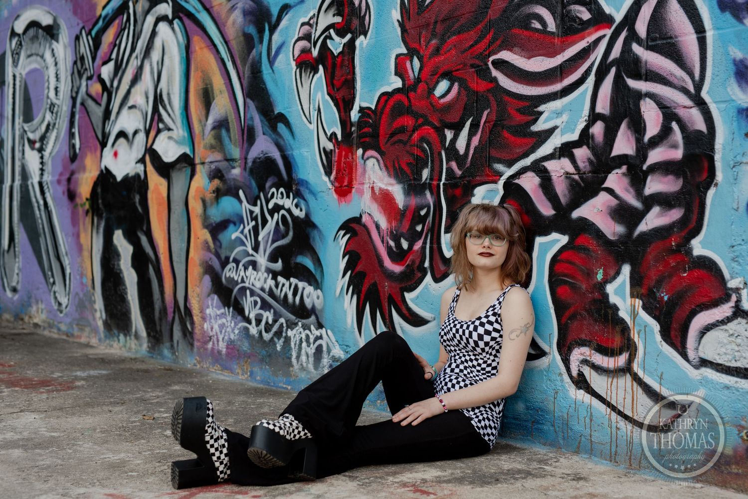A relaxed pose by artistic graffiti mural featuring red dragon design.