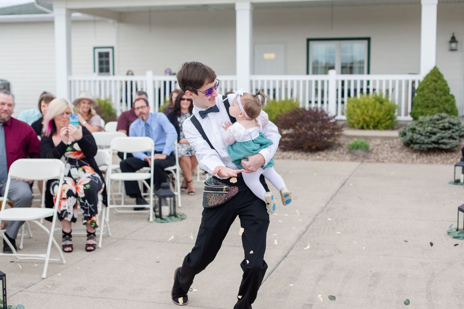 Wedding guests gather on a white columned porch during an outdoor celebration.