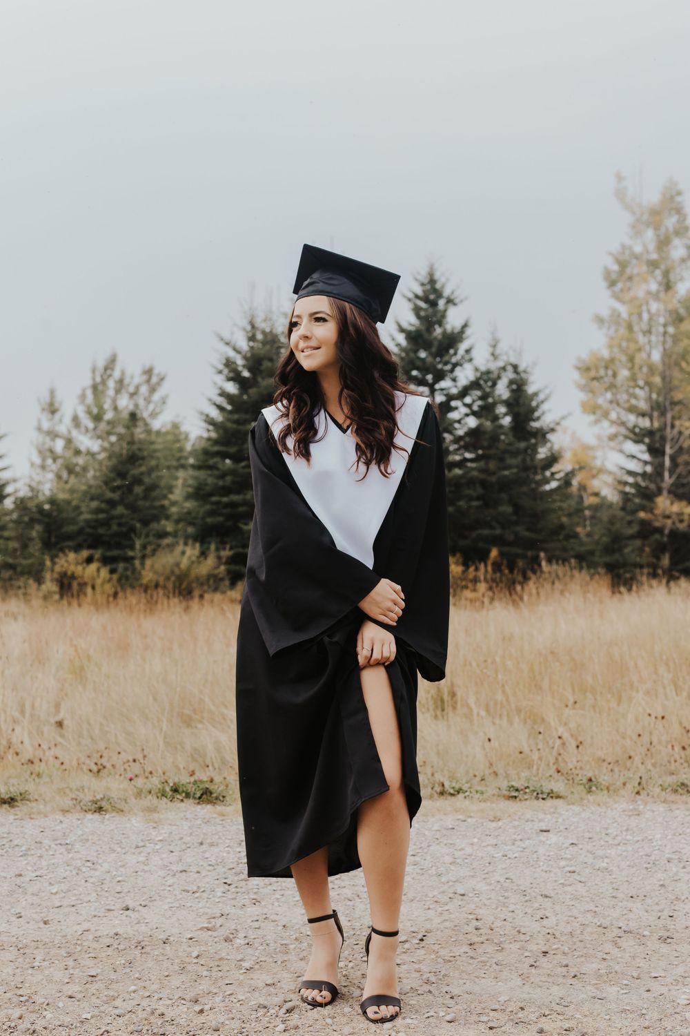 Girl in cap and gown lifts gown while gazing sideways