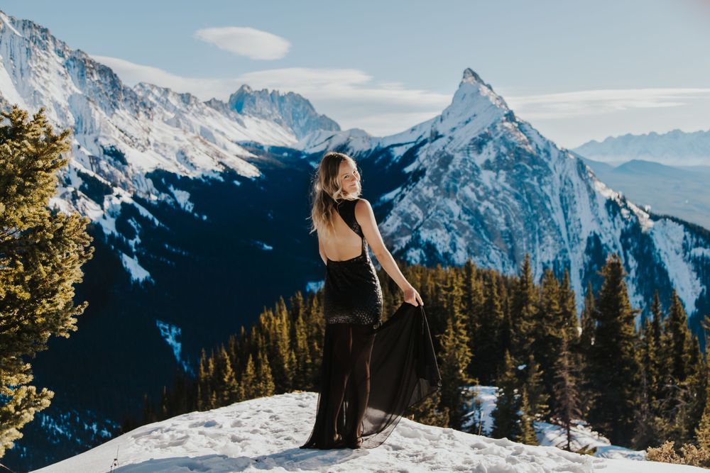 Girl in black dress looks over shoulder in front of mountains