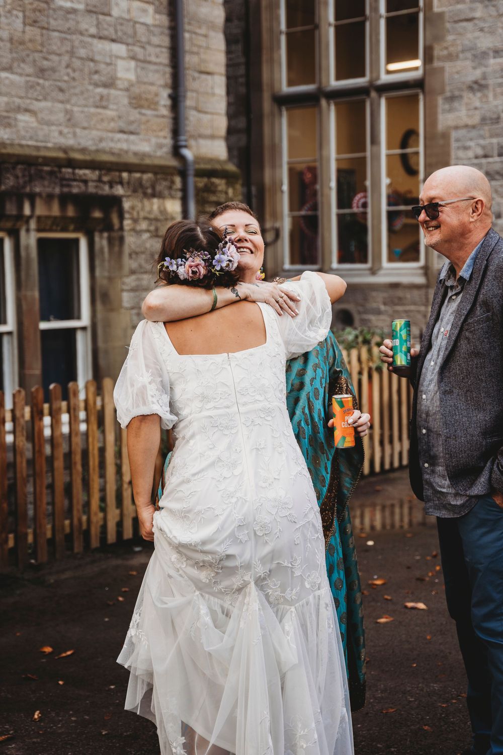 Wedding guests sharing embraces outside stone building during celebration.