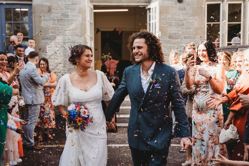 Joyful wedding exit with guests throwing confetti outside stone venue.