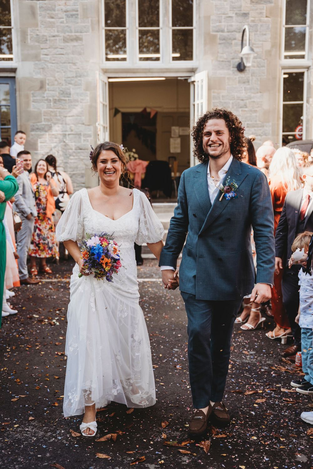 Wedding celebration with confetti toss outside historic stone building.