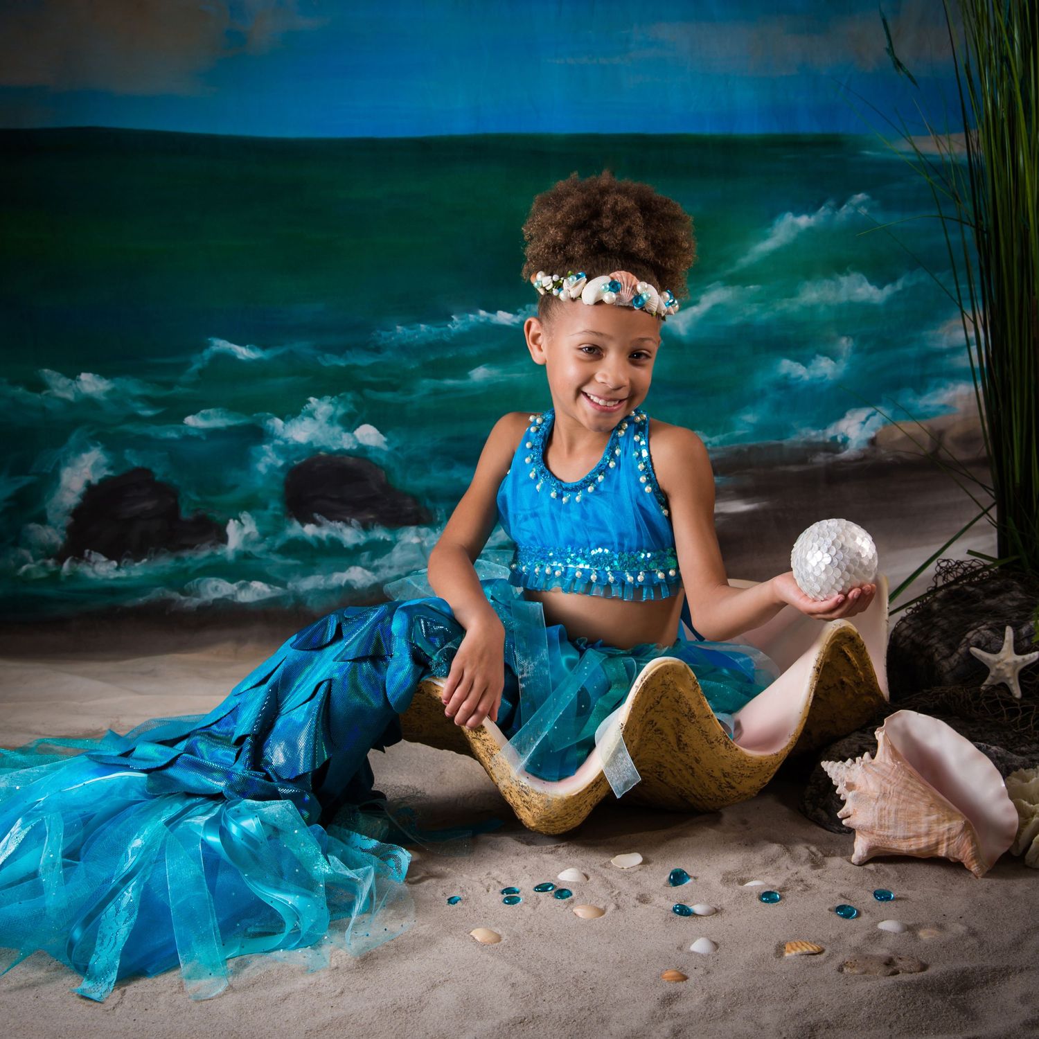 Beach photography series showing someone in a bright blue dress posing with seashells on sandy shore.
