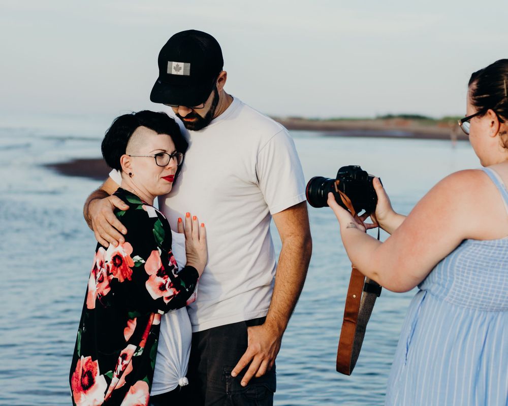 A photographer captures a candid moment by the water during a photoshoot at sunset.