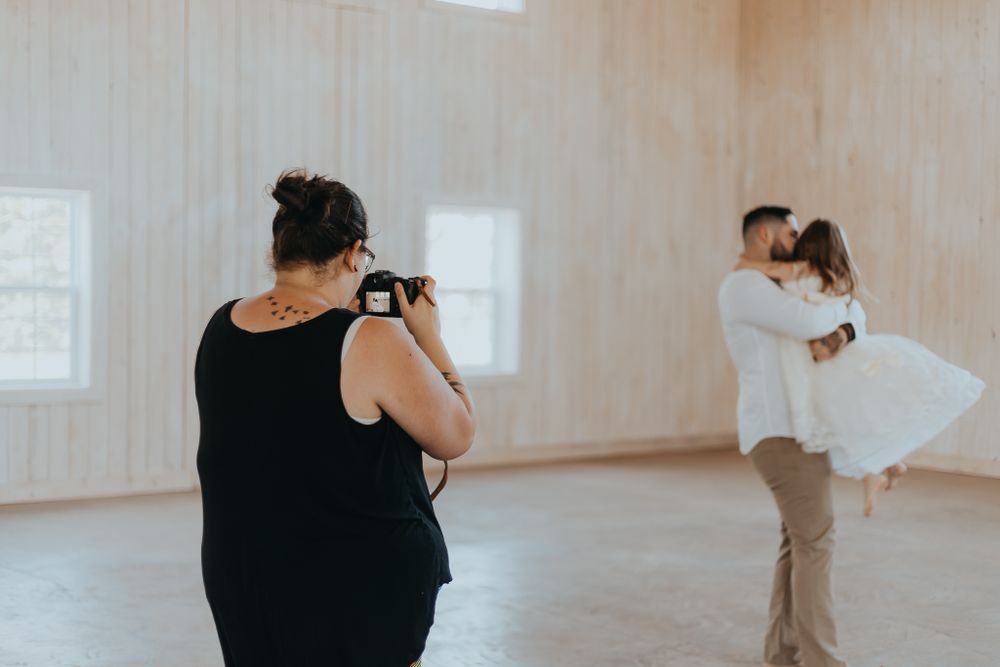 A photographer takes pictures of a couple in a bright studio with wooden floors.