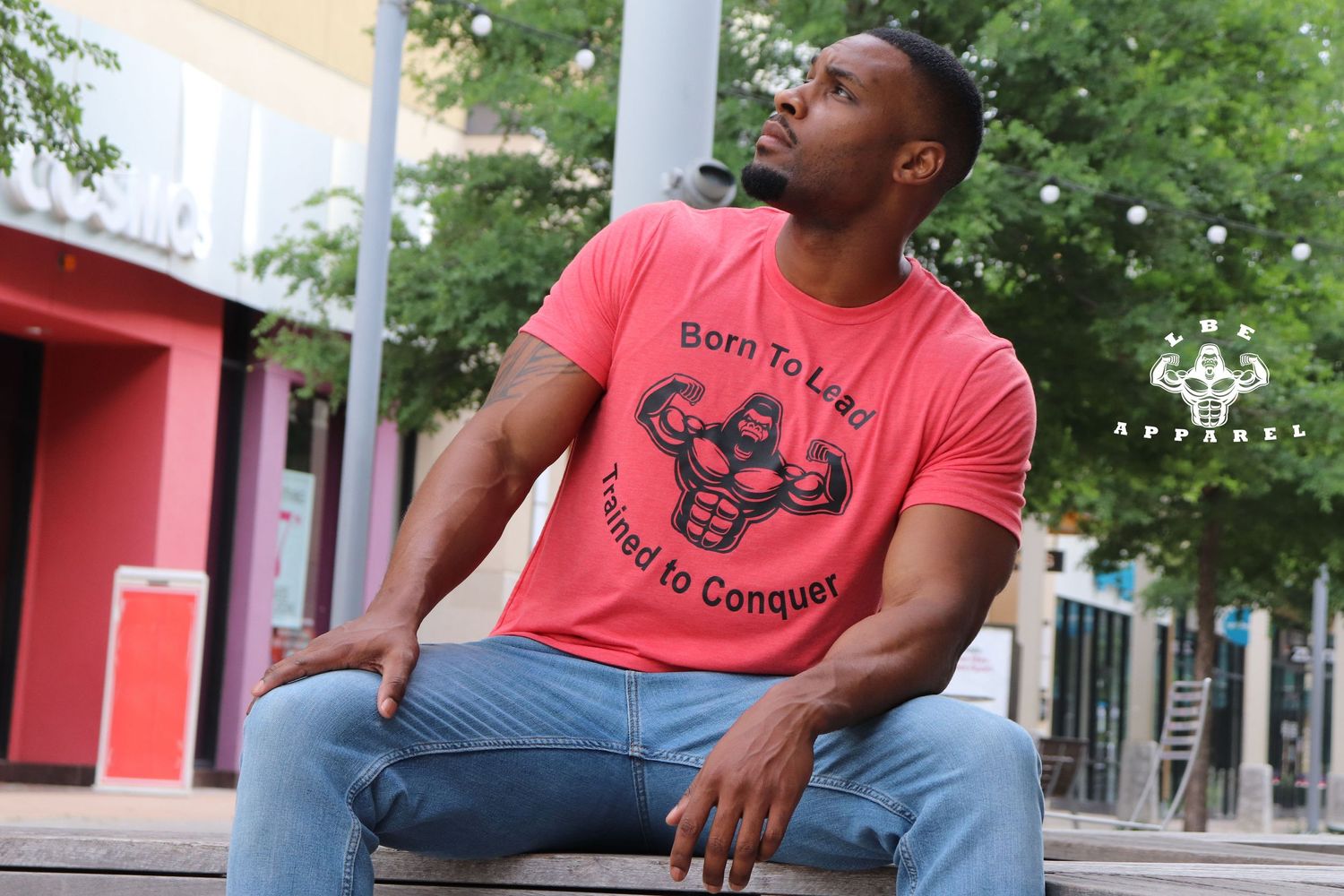Person in coral t-shirt with fitness design sitting outdoors looking to the side.