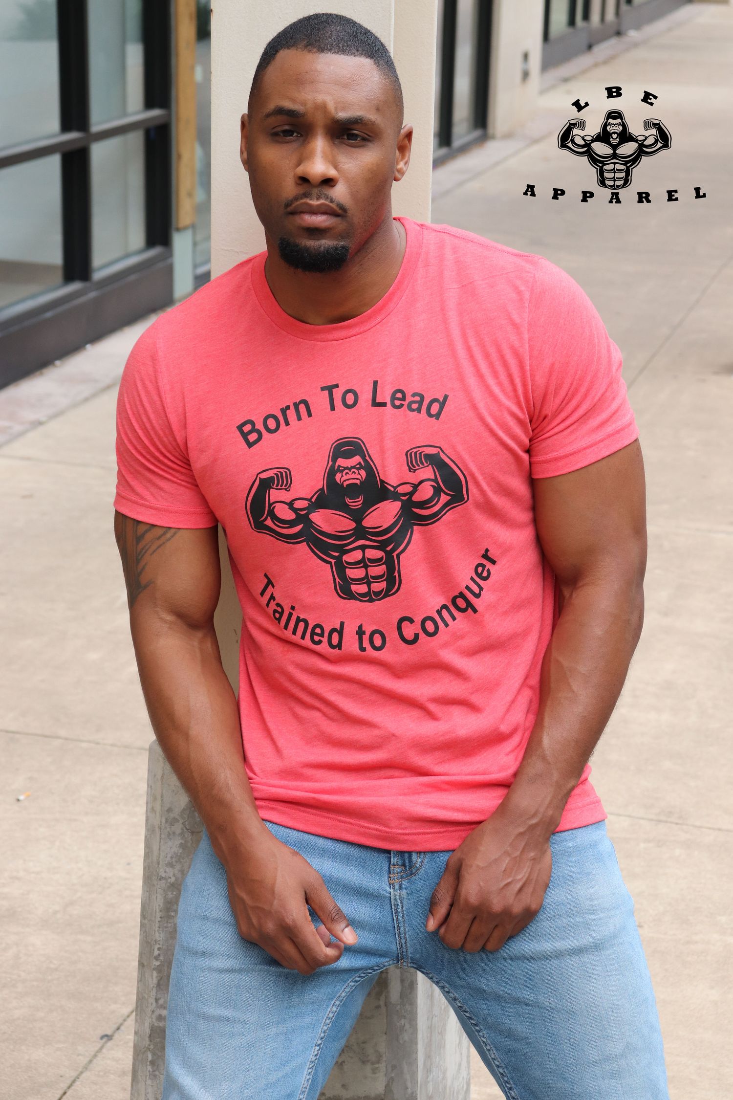 Athletic model wearing coral 'Born to Lead' t-shirt with fitness graphic against urban backdrop.