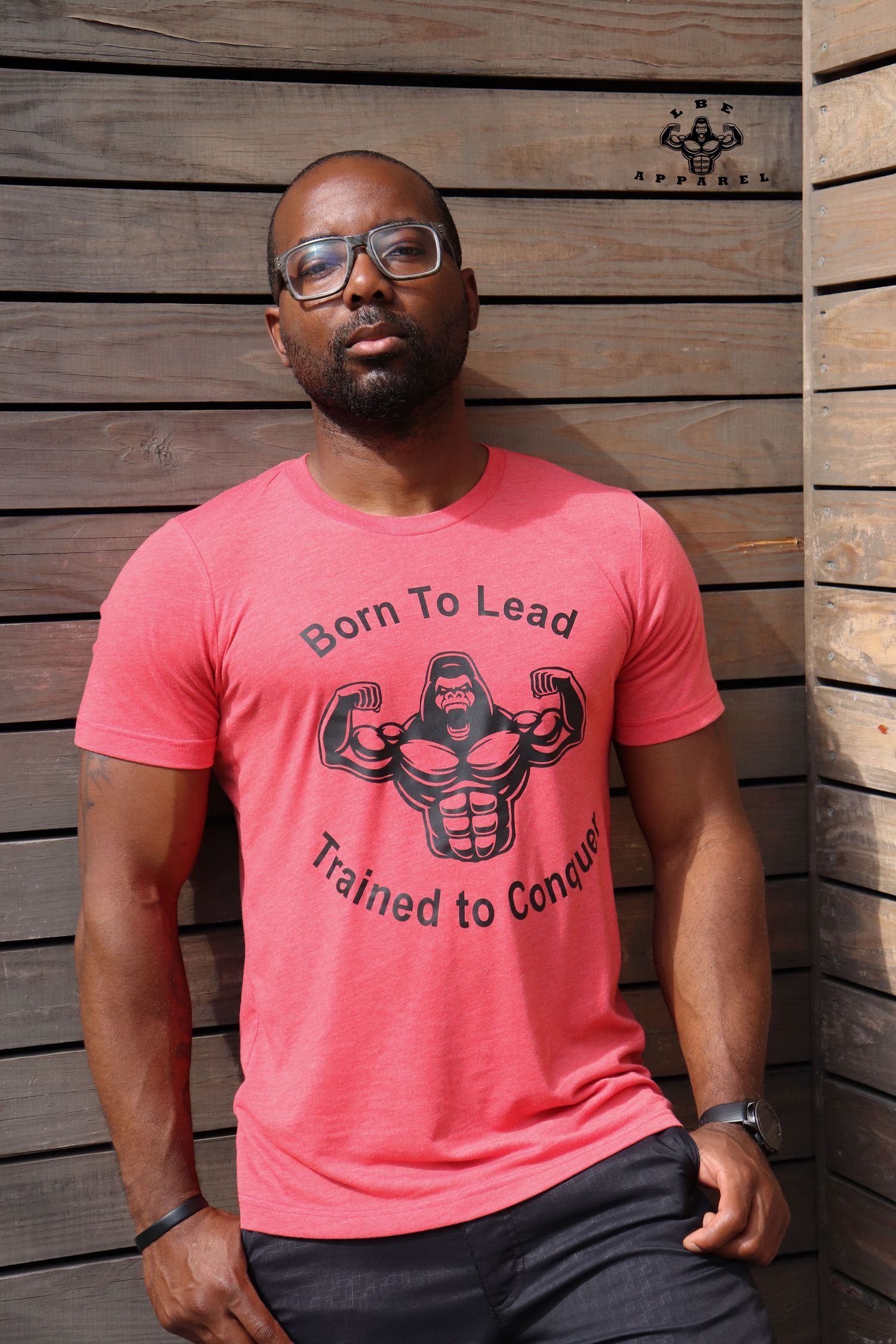 Portrait against wooden wall wearing coral fitness-themed t-shirt and glasses.