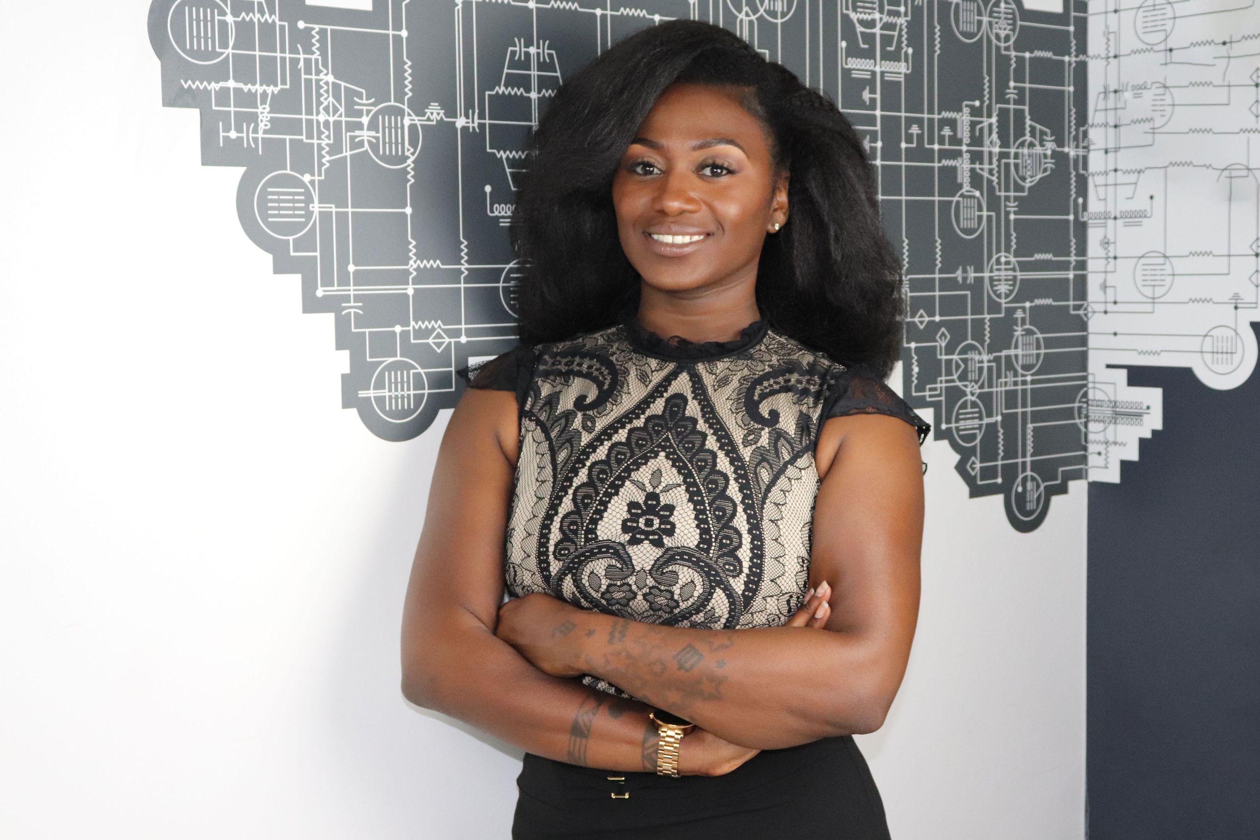 Professional portrait against geometric wall design wearing elegant black and beige top.