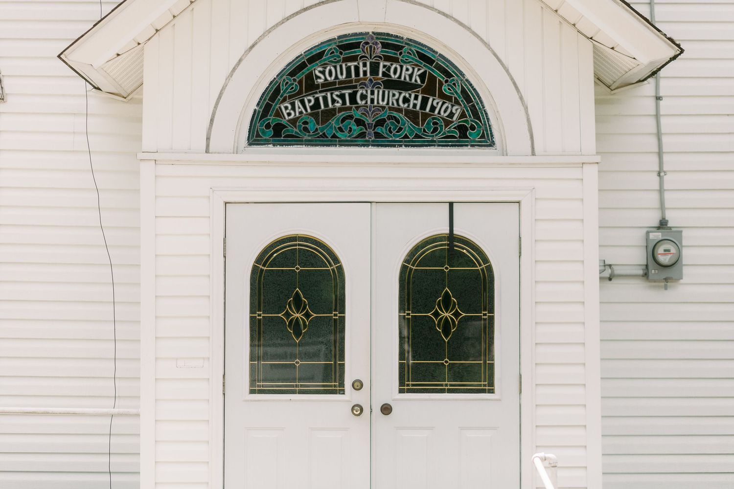 Close-up of white church facade with arched doorway and decorative green stained glass window.