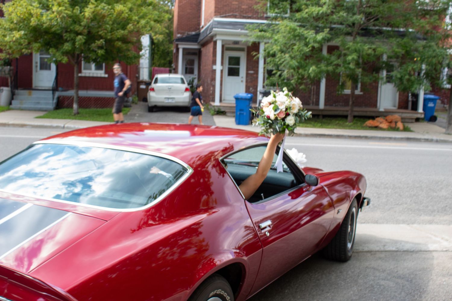 A red classic car decorated with a wedding bouquet parked on a residential street.