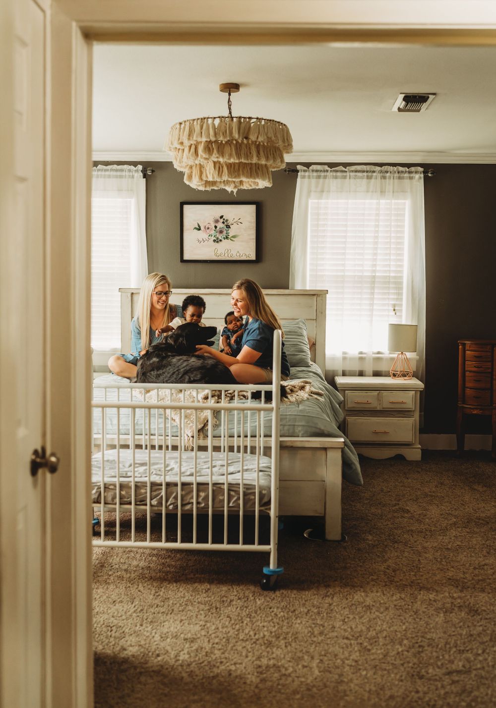 View through doorway of nursery room with crib and family relaxing on bed.