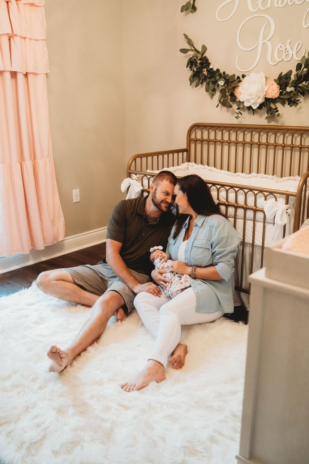Family sitting together on floor of nursery decorated with floral garland and pink curtains.