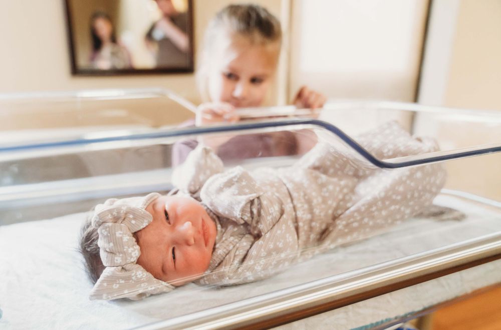 Newborn baby swaddled in beige blanket lying in hospital bassinet with monitor in background. fresh 48 Alexandria,la cabrini hospital